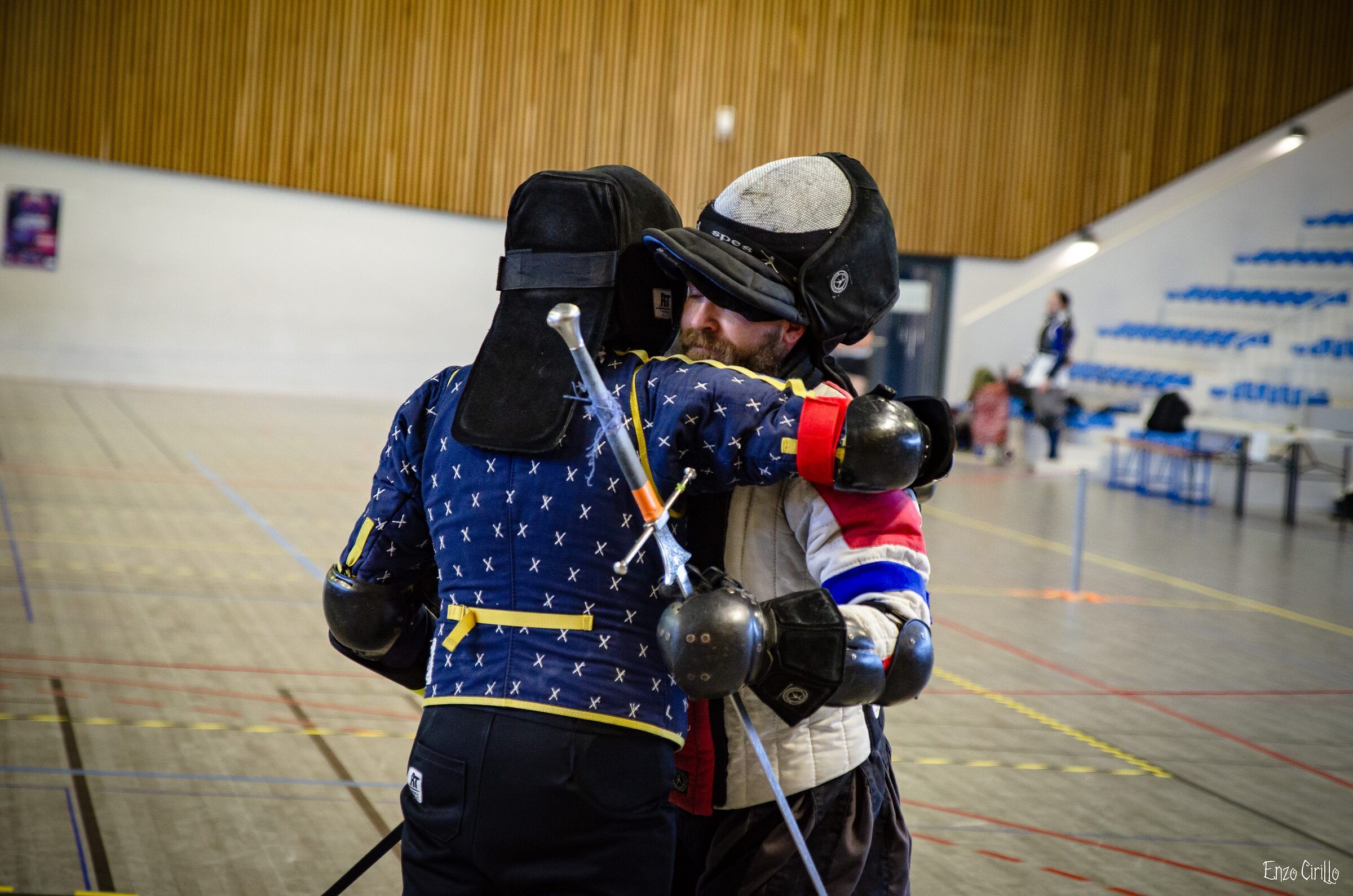 Deux escrimeurs en doublets bleu et blanc au corps-à-corps dans un gymnase.